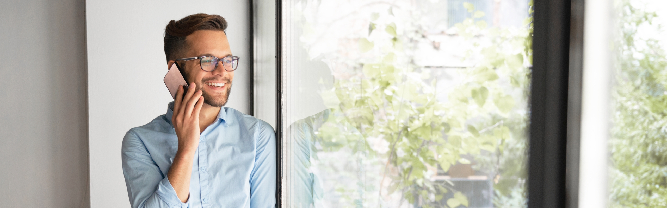 Mann telefoniert, lächelt und schaut in seinen grünen Garten