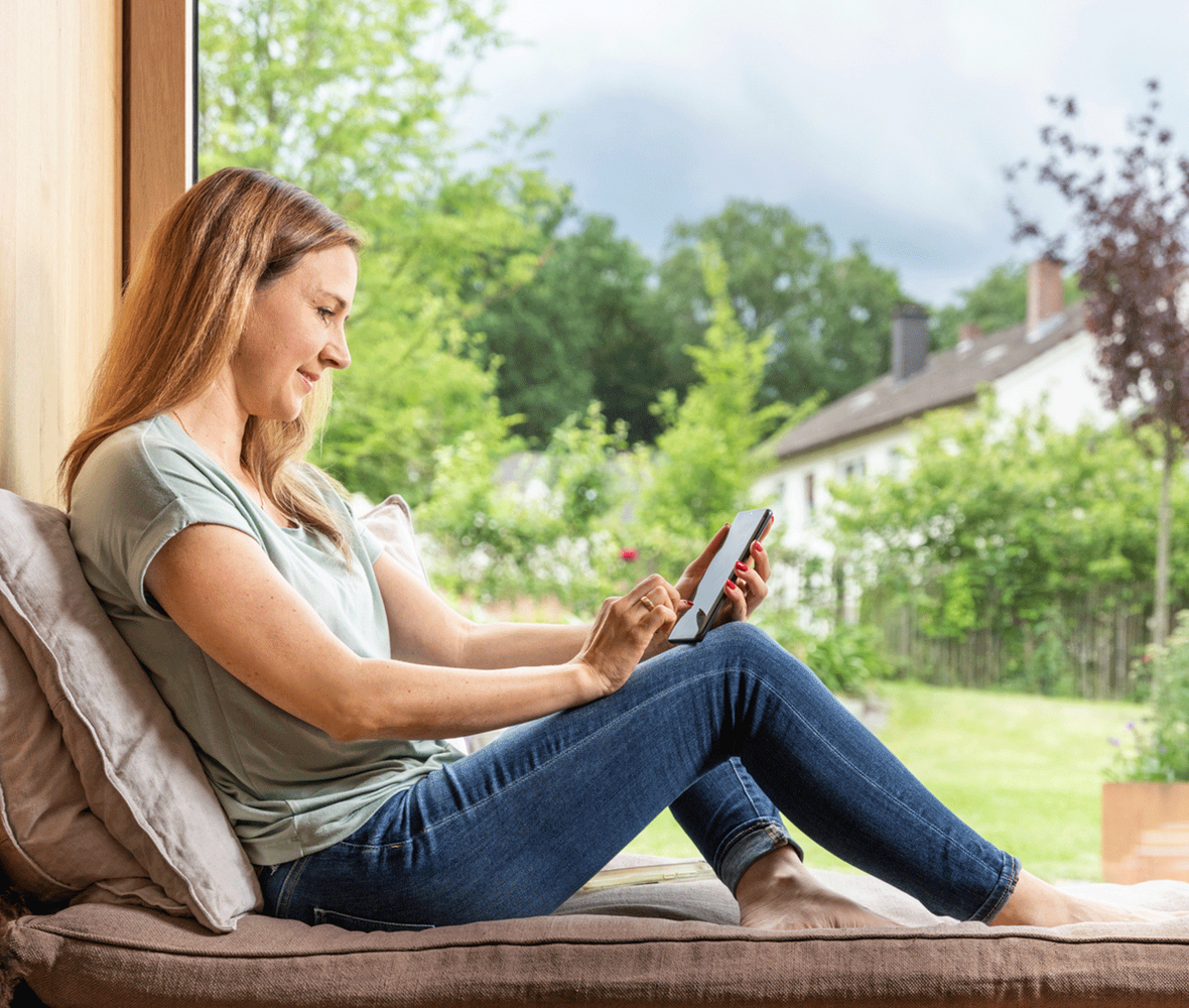 Frau sitzt auf Fensterbank und informiert sich am Handy
