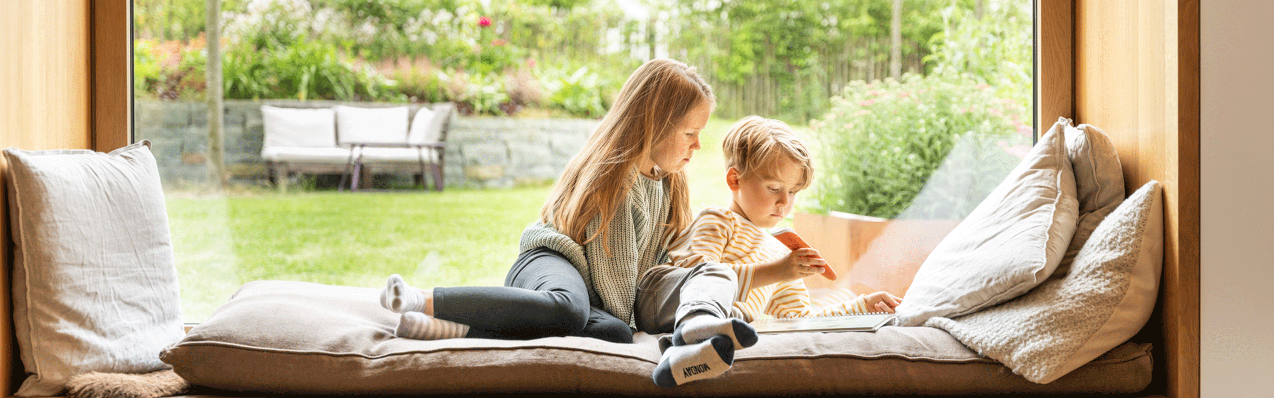 Bruder und Schwester sitzen auf Fensterbank und malen
